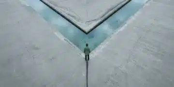 Navigating the New Normal: A Comparative Analysis of Evolving Societal Trends Aerial view of a person in a green rain jacket observing a geometrically reshaped riverbed, symbolizing societal shifts and changing courses.